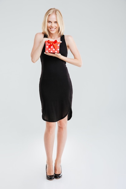 Ritratto integrale di una donna sorridente in regalo della holding del vestito nero isolato su una priorità bassa bianca