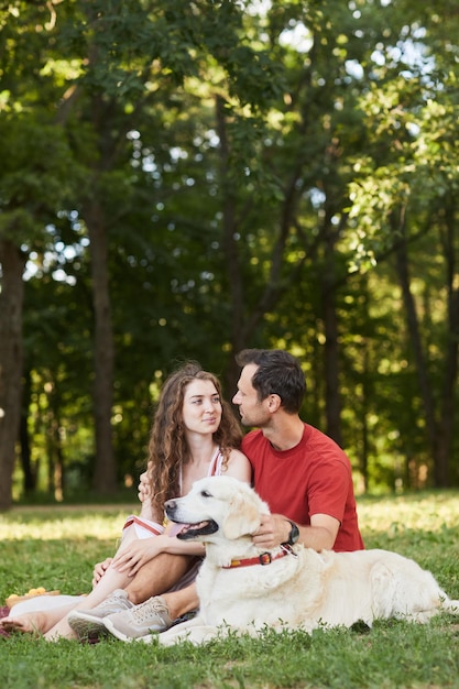 Ritratto integrale verticale di giovane coppia con il cane che gode del picnic all'aperto su erba verde