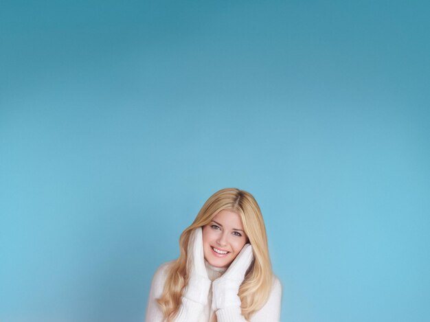 Ritratto invernale su sfondo blu donna bionda felice che indossa guanti caldi e maglione a maglia
