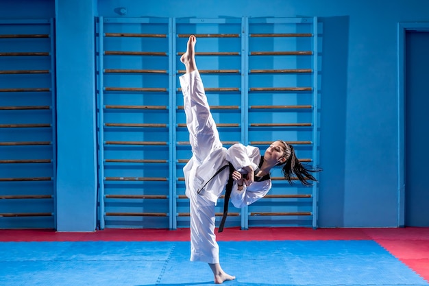 Ritratto isolato a figura intera di una bella donna di arti marziali in kimono che esercita il taekwondo di karate