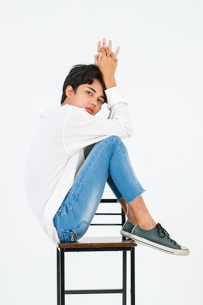 Ritratto isolato girato in studio Asian giovane LGBT gay felice bello bisessuale omosessuale modello di moda maschile in abito casual seduta gambe incrociate sulla sedia alta sorridente guardare la fotocamera su sfondo bianco