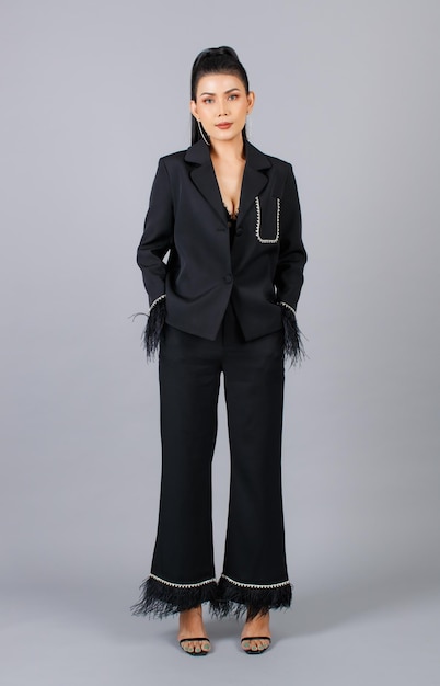 Ritratto isolato ritaglio studio colpo di Millennial Asian femminile elegante modella in nero casual vestito di pelliccia alla moda in piedi in posa mettere mano nella tasca dei pantaloni guarda la fotocamera su sfondo grigio