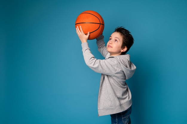 Ritratto isolato su sfondo blu di un bel ragazzo che gioca a basket. Bambino sportivo che gioca a basket.