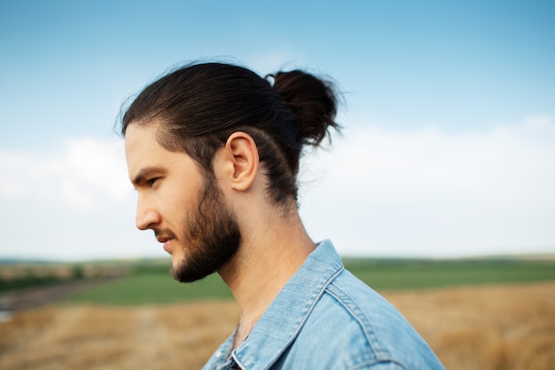 Ritratto laterale del primo piano di giovane ragazzo hipster con l'acconciatura a coda di cavallo.