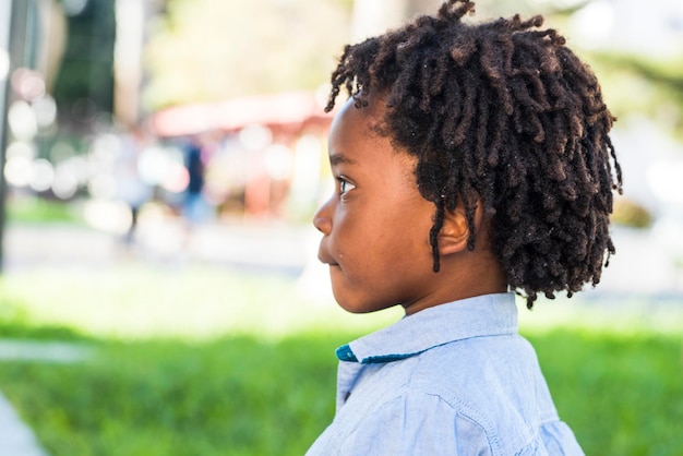 Ritratto laterale di bambini piccoli diversità afroamericana etica nera con parco giochi verde sullo sfondo Dredd capelli stile ragazzino da solo vista laterale