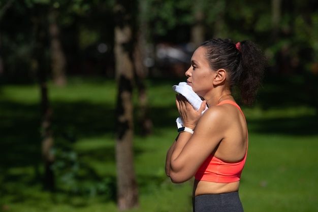 Ritratto laterale di giovane donna stanca asciugandosi il sudore dopo aver eseguito l'allenamento. Allenamento cardio all'aperto