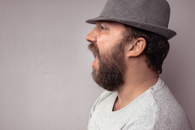 Ritratto laterale di un uomo barbuto che grida Ritratto di un uomo barbuto arrabbiato contro un muro grigio