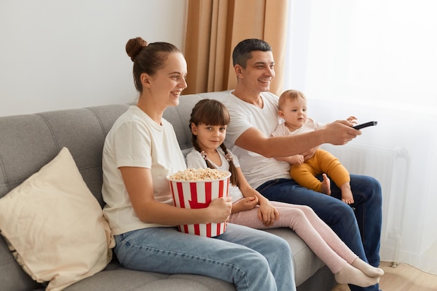 Ritratto laterale di una famiglia felice seduta sul divano e guardando film con popcorn che esprimono emozioni positive mentre si guarda la tv insieme godendosi il tempo libero