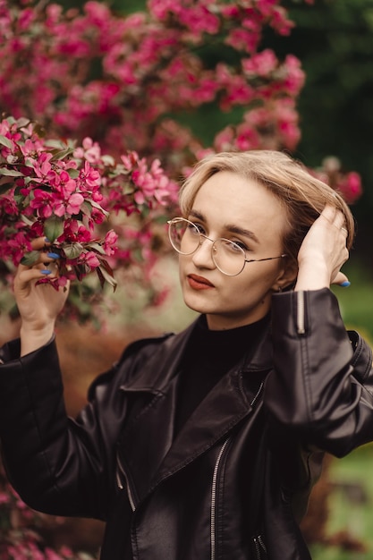 Ritratto luminoso di una giovane ragazza bionda felice in nero sullo sfondo di un albero di fiori rosa in autunno