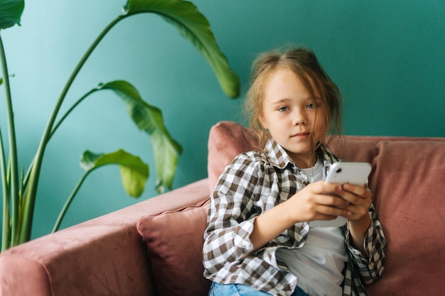 Ritratto medio di una bambina abbastanza adorabile che utilizza smartphone che guarda l'obbiettivo