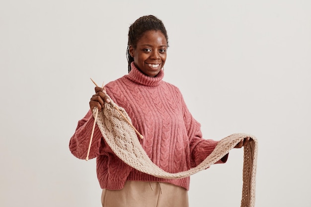 Ritratto minimale in vita di giovane donna afroamericana che tiene sciarpa lavorata a maglia e sorride alla macchina...