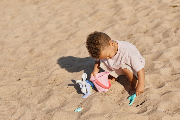 Ritratto minimo ad alto angolo di un bambino carino che gioca nella sabbia in spiaggia allo spazio della copia del sole