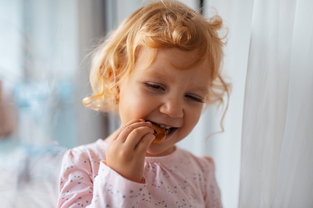 Ritratto naturale del primo piano del bambino che mangia bagel a casa.