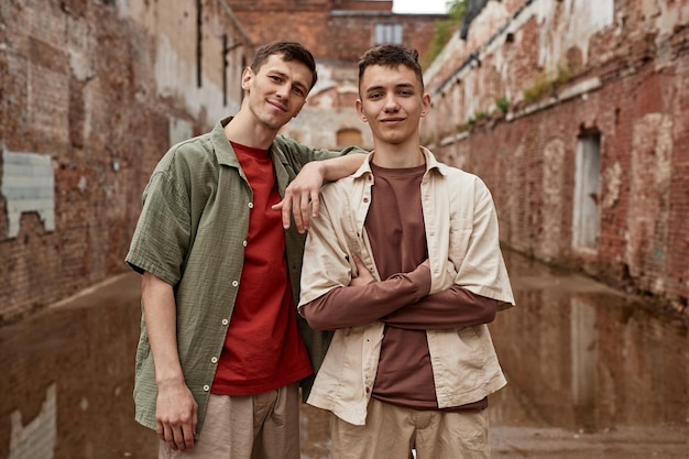 Ritratto neutro in vita di due ragazzi gemelli che guardano la fotocamera in un ambiente urbano squallido con muro di mattoni