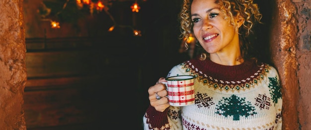 Ritratto orizzontale di attraente donna di mezza età che sorride e prende una tazza di tè nel periodo natalizio a casa Le persone felici si godono la celebrazione delle vacanze di Natale Copia l'immagine dello spazio per il mese di dicembre