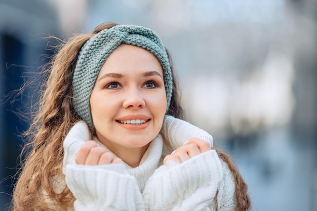 Ritratto per strada su sfondo sfocato. Giovane ragazza in abito freddo si alza e guarda qualcosa con uno sguardo ammirato e interessato. Sorriso gioioso ed entusiasta. Il concetto di osservare qualcosa.