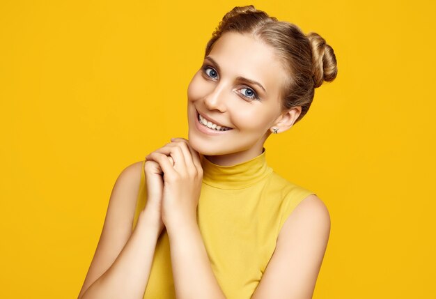 Ritratto positivo del modello di donna splendida bionda hipster con capelli ricci in posa su sfondo colorato giallo in studio