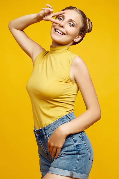 Ritratto positivo del modello di donna splendida bionda hipster con capelli ricci in posa su sfondo colorato giallo in studio