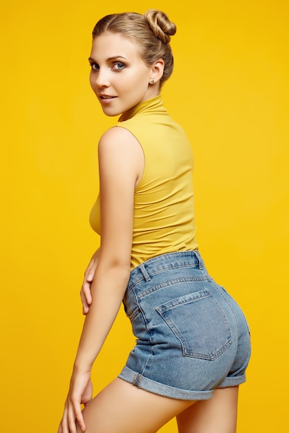 Ritratto positivo del modello di donna splendida bionda hipster con capelli ricci in posa su sfondo colorato giallo in studio