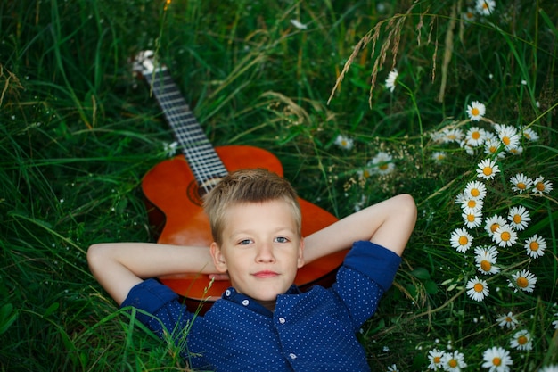 Ritratto ragazzo adolescente sdraiato sull&#39;erba con la sua chitarra acustica.