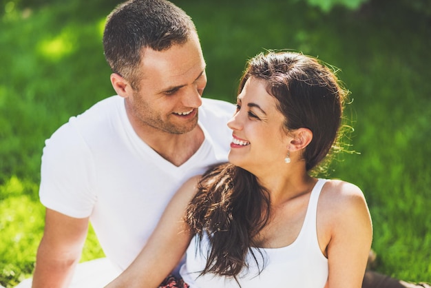 Ritratto ravvicinato di bella coppia innamorata seduta su una coperta da picnic all'aperto Caucasico felice uomo sognante e sorridente donna bruna seduta sull'erba verde nel parco che si guardano l'un l'altro