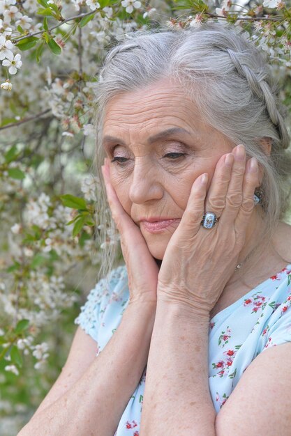 Ritratto ravvicinato di donna anziana triste vicino a un albero primaverile in fiore