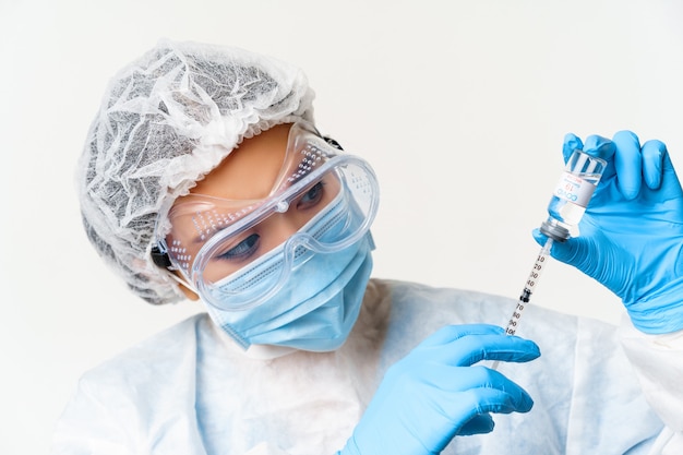 Ritratto ravvicinato di dottoressa o infermiera asiatica in dispositivi di protezione individuale, vaccinazione dal coronavirus, riempimento della siringa con vaccino covid-19, sfondo bianco