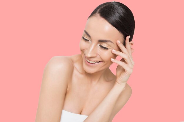 Ritratto ravvicinato di giovane donna con viso di bellezza e pelle del viso sana Modello di bella ragazza sorridente con trucco naturale che tocca la pelle idratata e luminosa Cosmetologia bellezza e cura della pelle Spa