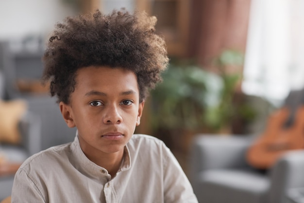 Ritratto ravvicinato di un adolescente afro-americano che guarda la telecamera mentre posa in un interno minimo di casa, copia spazio