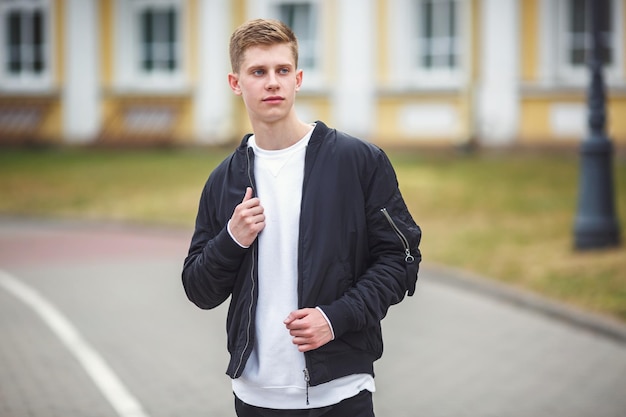 Ritratto ravvicinato di un bel ragazzo adolescente con una giacca sulla spalla in una strada urbana sullo sfondo