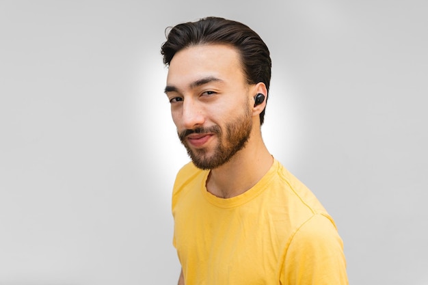 Ritratto ravvicinato di un giovane latino di profilo sorridente con auricolari wireless guardando lo sfondo bianco con sicurezza della fotocamera