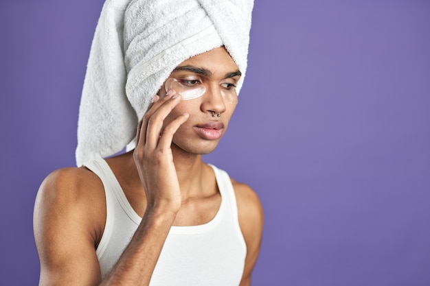 Ritratto ravvicinato di un giovane uomo latinoamericano in un asciugamano applicato sotto i cerotti di collagene per gli occhi
