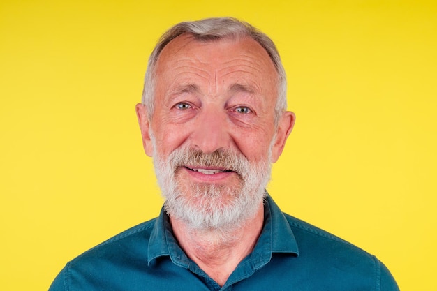 Ritratto ravvicinato di un uomo anziano felice che guarda la fotocamera, indossando una camicia di cotone verde con colletto su sfondo giallo da studio.