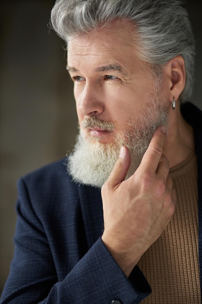 Ritratto ravvicinato di un uomo di mezza età dai capelli grigi elegante e bello che distoglie lo sguardo toccando il suo