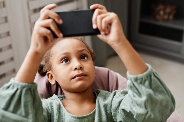 Ritratto ravvicinato di una bambina afroamericana che utilizza lo spazio della copia dello smartphone a casa