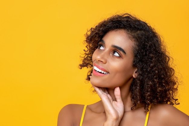 Ritratto ravvicinato di una bella donna americana Afican sorridente che pensa guardando in alto isolato su sfondo giallo