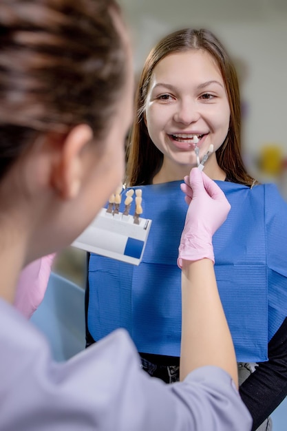 Ritratto ravvicinato di una bella giovane donna seduta sulla poltrona del dentista mentre lo stomatologo indossa guanti sterili che tengono campioni di denti.