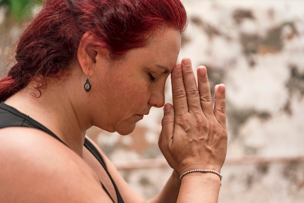Ritratto ravvicinato di una donna meditante dai capelli rossi che si tiene per mano in una posizione namaste
