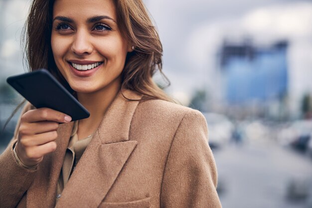 Ritratto ravvicinato di una donna sorridente che utilizza la modalità altoparlante sul suo gadget durante la conversazione