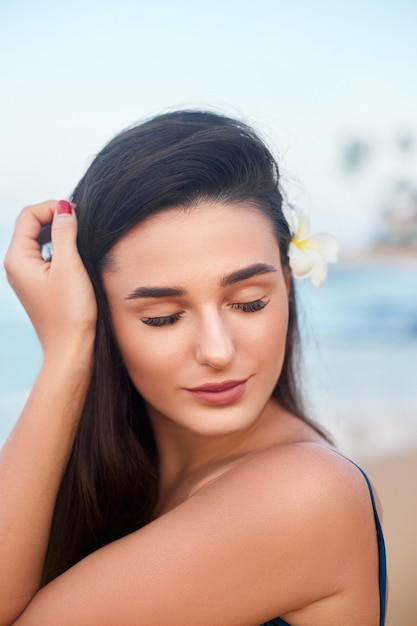 Ritratto ravvicinato di una donna sorridente in riva al mare con un fiore tra i capelli