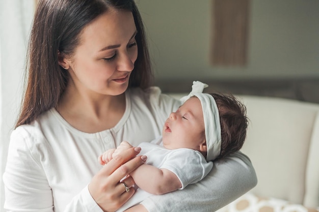 Ritratto ravvicinato di una piccola neonata carina dai capelli scuri in un abito bianco tra le braccia di una giovane madre Genitore di maternità Sonno sano