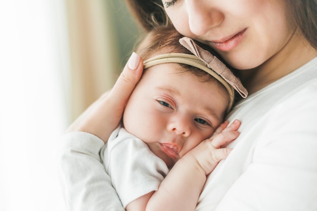 Ritratto ravvicinato di una piccola neonata carina dai capelli scuri in un abito bianco tra le braccia di una giovane madre Genitore di maternità Sonno sano