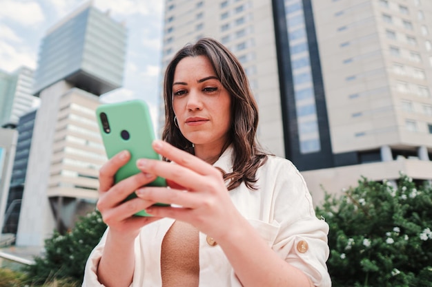 Ritratto ravvicinato di una ragazza caucasica bruna che guarda le notizie concentrate su un'app per smartphone Giovane donna caucasica seria che utilizza un cellulare in piedi all'aperto