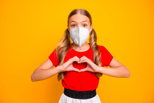 Ritratto ravvicinato lei ragazza sana e attraente che indossa una maschera respiratore di sicurezza che mostra la forma del cuore fermare la malattia influenzale immunità isolata brillante vivido brillantezza vibrante colore giallo sfondo