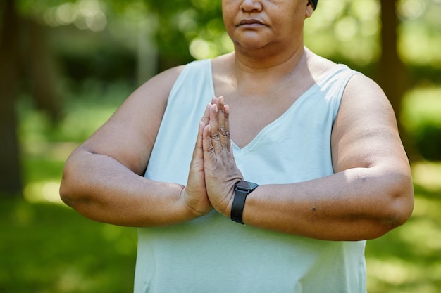 Ritratto ritagliato di donna nera matura che fa yoga all'aperto nel parco verde e si tiene per mano insieme
