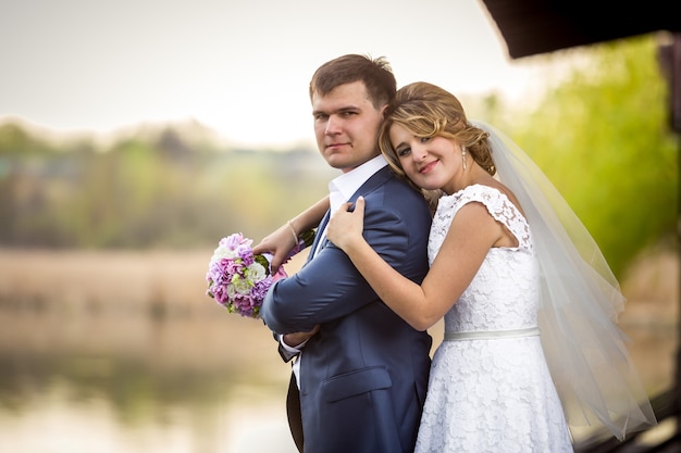 Ritratto romantico di bella sposa che abbraccia la spalla degli sposi al lago