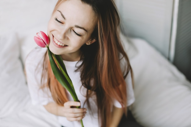 Ritratto romantico di una bellissima giovane donna con fiori di tulipano a letto