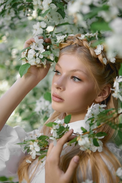 Ritratto romantico di una ragazza nel parco vicino a un melo in fiore. Cosmetici naturali. Bellezza naturale di una donna in abito bianco