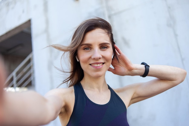 Ritratto selfie di una bella donna in fitness con le cuffie in un luogo urbano