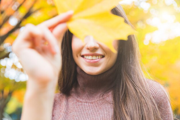 Ritratto sorridente della donna con una foglia gialla in autunno